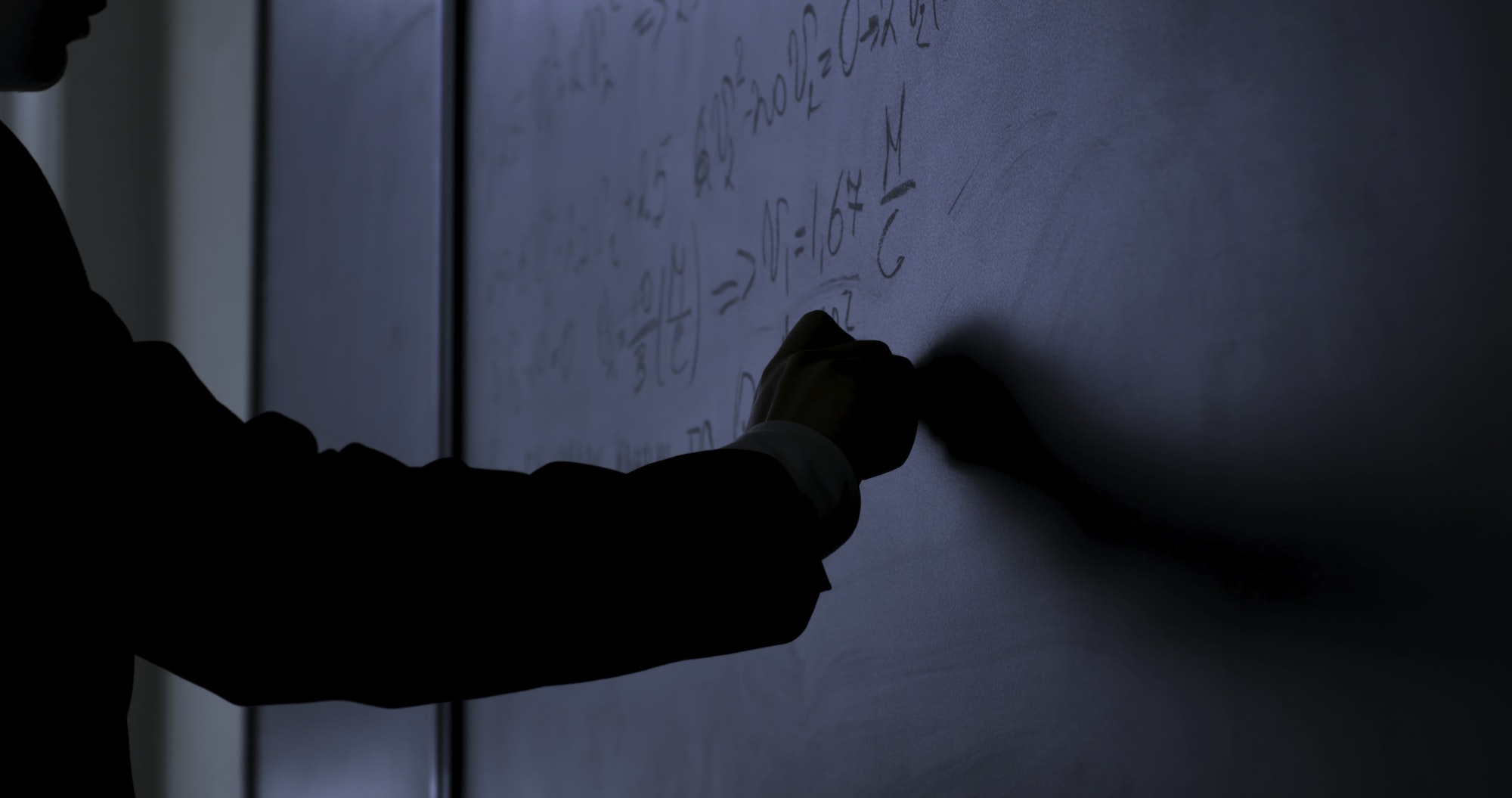 Scientist writing formulas on chalkboard. Hand with chalk wrote physics formulas on black chalkboard